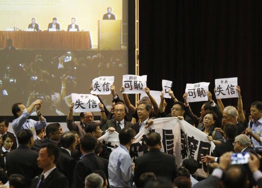 Pro-democracy lawmakers hold up a banner and signs during a protest as Li Fei (seen on screen), deputy general secretary of the National People's Congress (NPC) standing committee, speaks during a briefing session in Hong Kong