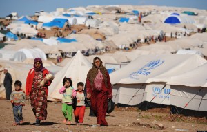 alt="Syrian internally displaced people walk in the Atme camp, along the Turkish border in the northwestern Syrian province of Idlib, on March 19, 2013. The conflict in Syria between rebel forces and pro-government troops has killed at least 70,000 people, and forced more than one million Syrians to seek refuge abroad"
