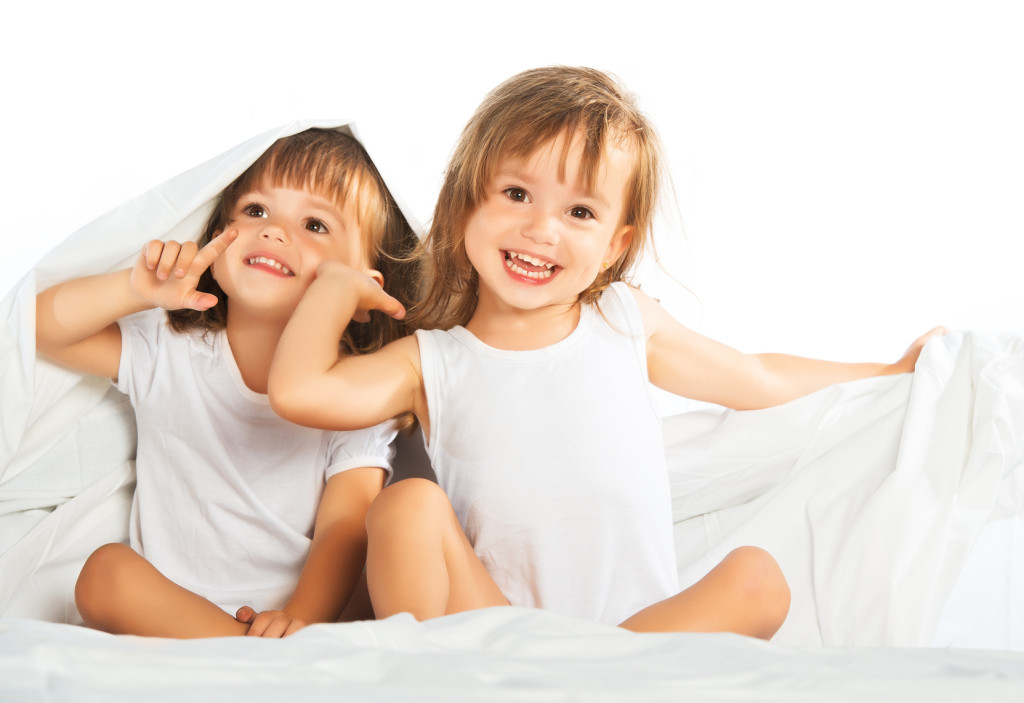 happy little girls twins sister in bed under the blanket having